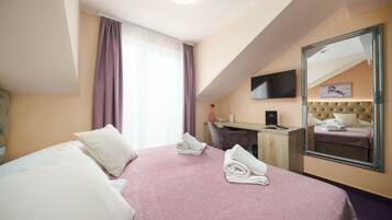 Una habitación de hotel con cama, escritorio, espejo y televisión.