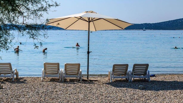 A beach with a row of sun loungers and a large umbrella providing shade. - Hotel Stella Maris (Vodice)