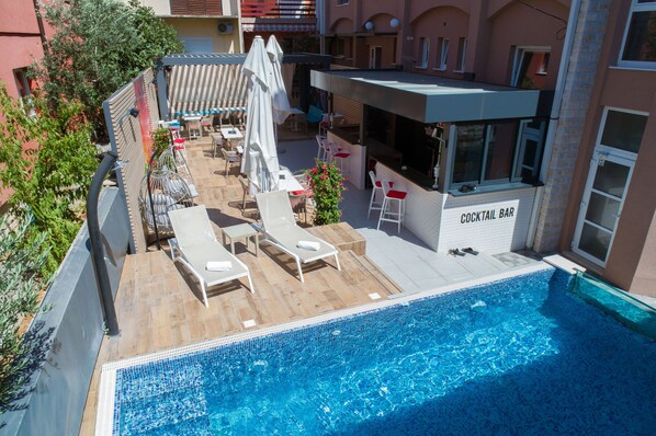 Zona de piscina en la azotea con sillones de descanso, un bar y vistas a la ciudad.