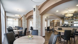 A restaurant with round tables, black chairs, and a bar area with shelves of bottles. - Hotel Stella Maris (Vodice)