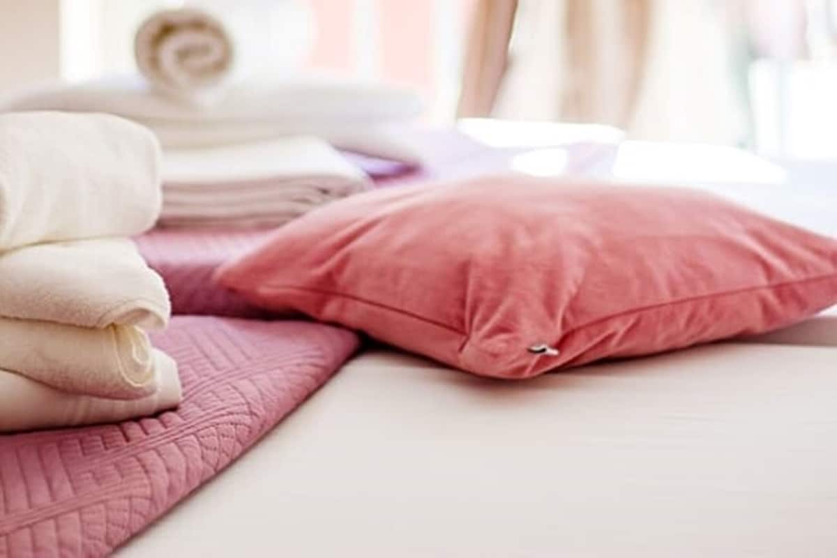 A neatly made bed with pink and white linens, a rolled white towel, and a pink pillow.