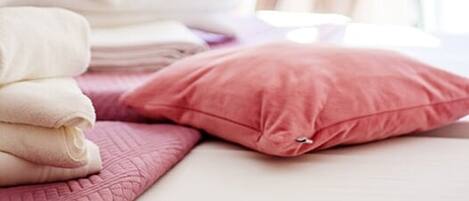 A neatly made bed with pink and white linens, a rolled white towel, and a pink pillow.