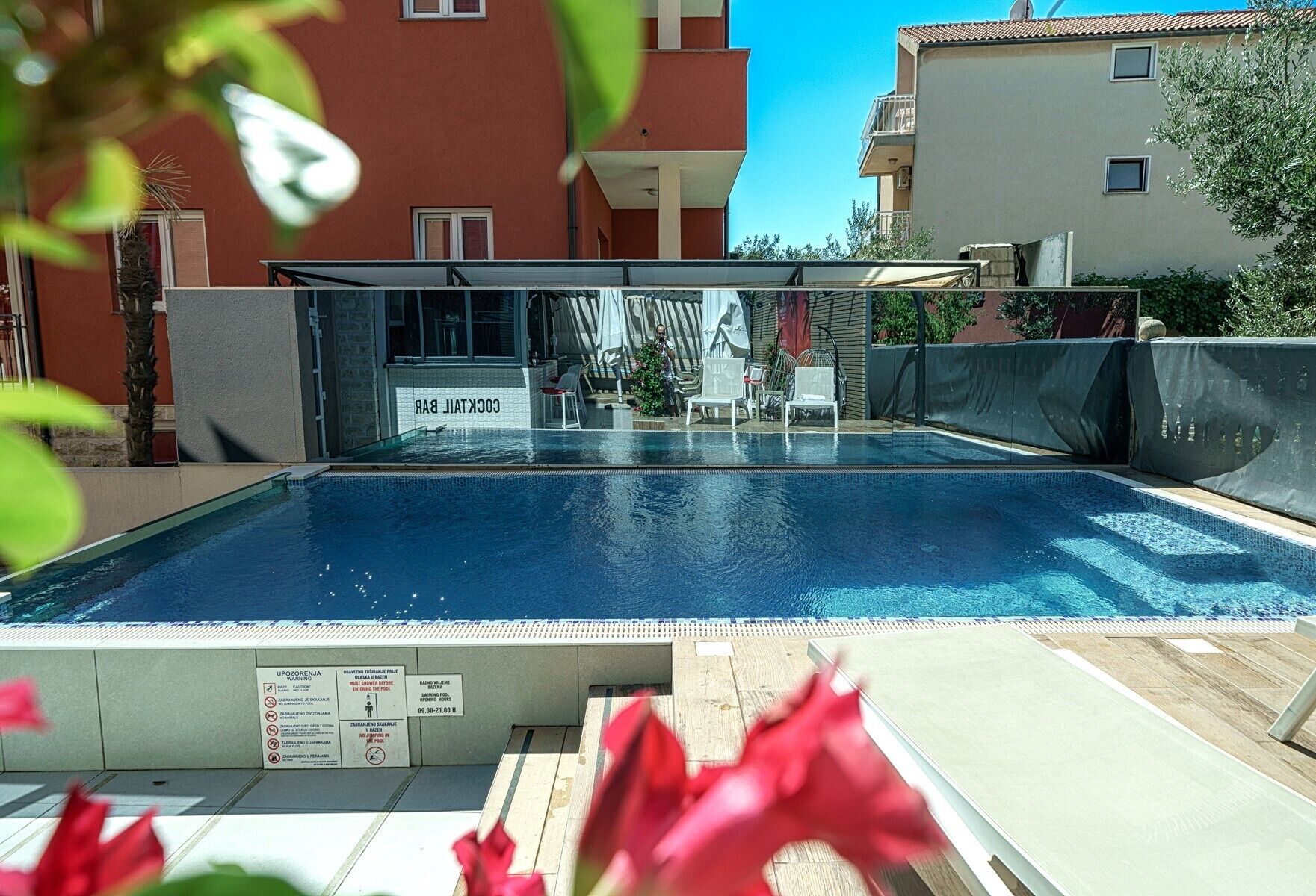 A swimming pool with a covered area, surrounded by buildings and a clear sky.