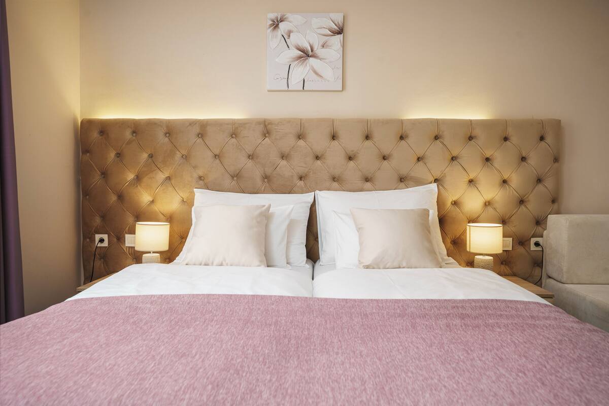 A double bed with a tufted headboard, two bedside lamps, and a pink blanket.