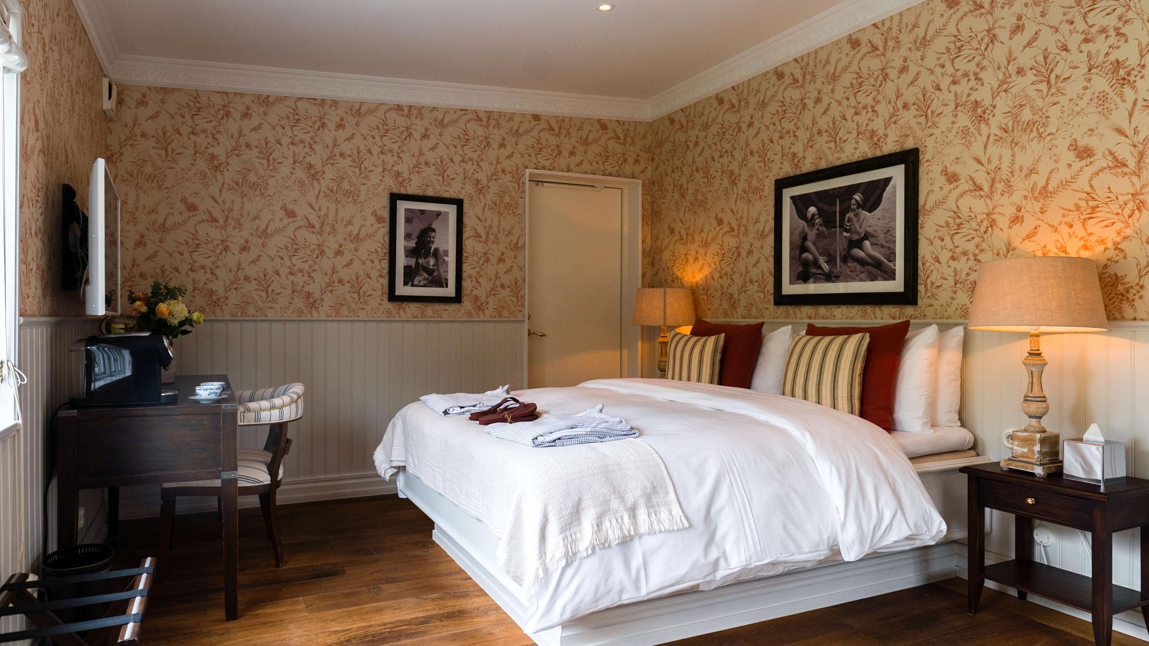 A neatly arranged bedroom with a bed, bedside tables, a desk, and a chair.