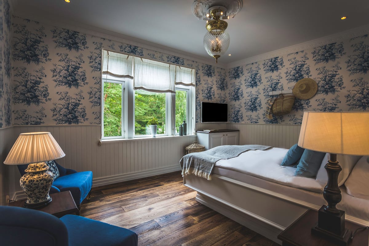 A bedroom with a bed, a TV, a window with curtains, a lamp, and a blue chair.