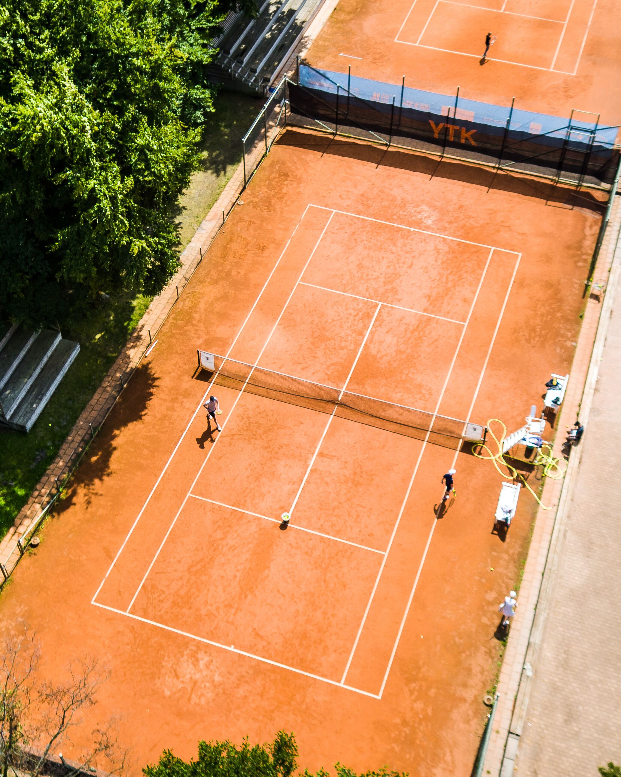 Vista aérea de una cancha de tenis con jugadores, una red y una valla.