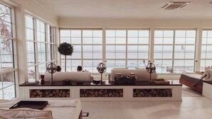 Une pièce spacieuse avec de grandes fenêtres donnant sur un paysage enneigé, un coin salon confortable avec une cheminée et un lit soigneusement fait.
