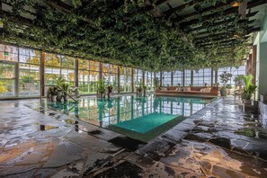 Una piscina interior con suelo de piedra, ventanas amplias y vegetación en el techo.