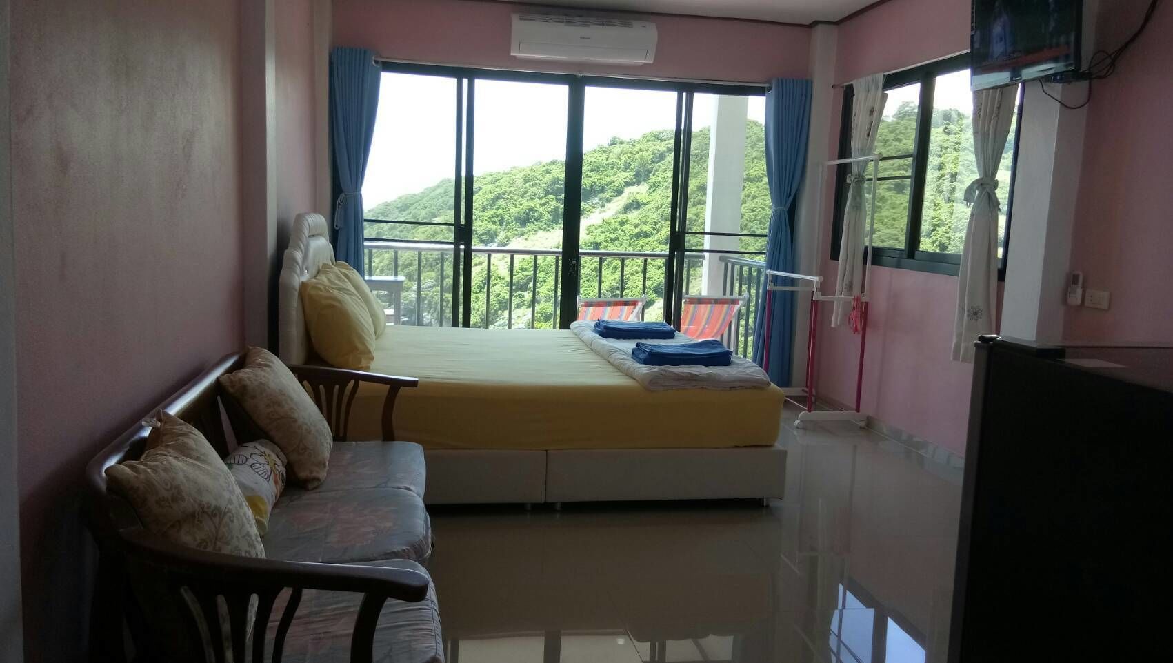 Quarto com cama, sofá e varanda com vista para colinas verdes.