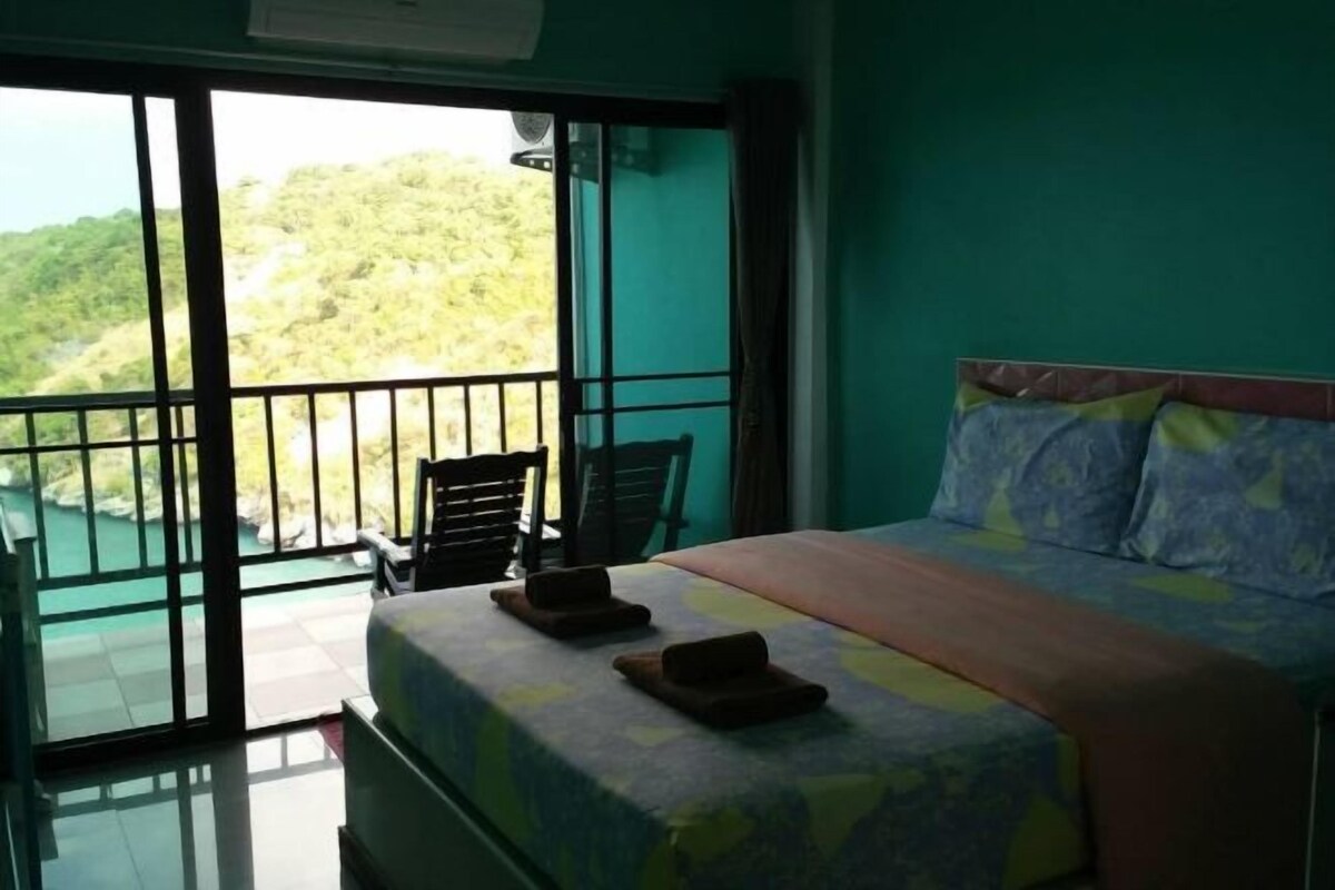 Una habitación con cama, una silla y un balcón con vistas a zonas verdes.