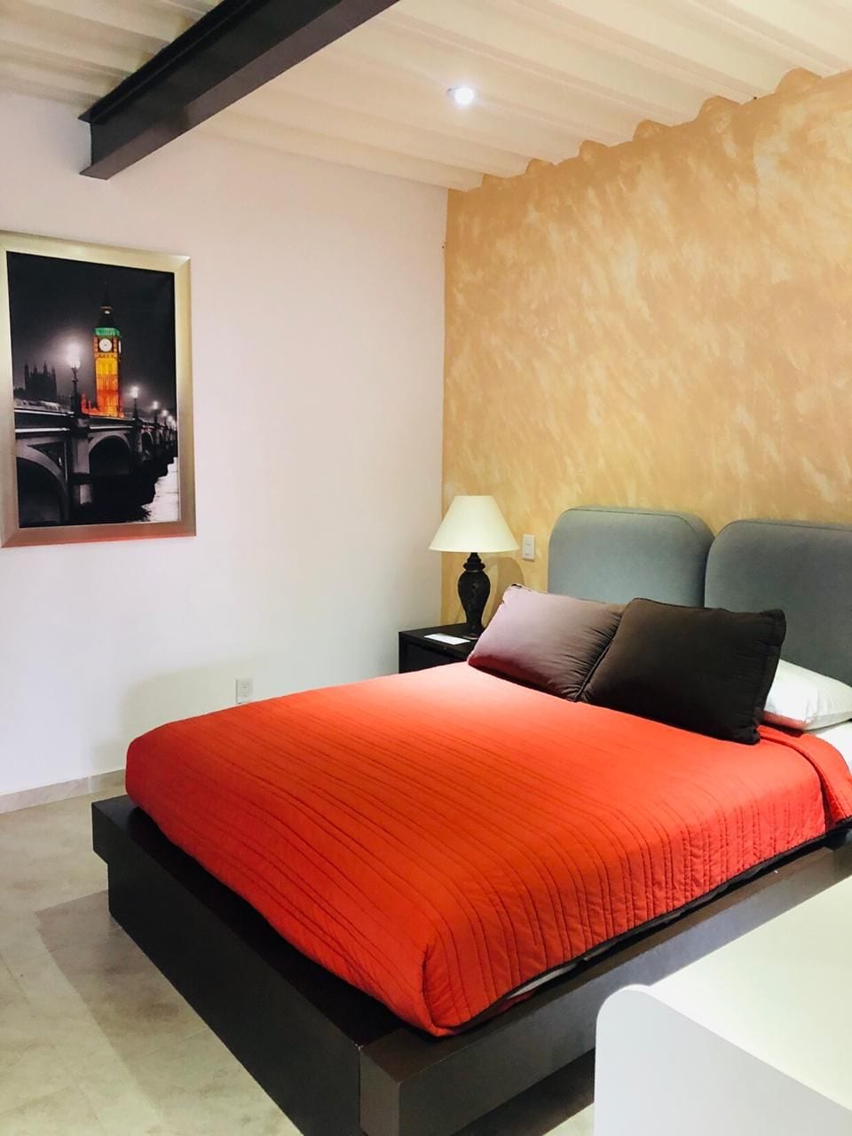 A hotel room with a bed, a nightstand, a lamp, and a framed picture on the wall.