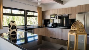 A modern kitchen with wooden cabinets, a black countertop, a microwave, a stove, and a refrigerator. - Vista Real Villas (Corregidora)