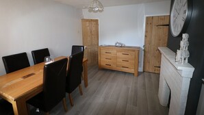 A dining area with a wooden table and chairs, a wooden cabinet, a clock, and a fireplace. - Victoria House (Colchester)