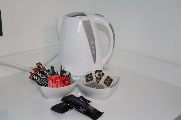A white kettle and two bowls filled with Nescafe coffee packets on a white countertop. - Victoria House (Colchester)