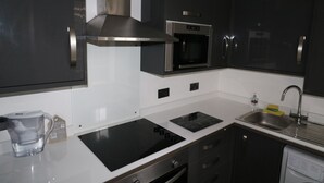 A modern kitchen with dark cabinets, a stainless steel range hood, a built-in microwave, a dishwasher, and a coffee maker. - Victoria House (Colchester)