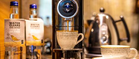 A coffee machine with a cup placed on its base, a coffee cup on a saucer, and two bottles of water on the counter.