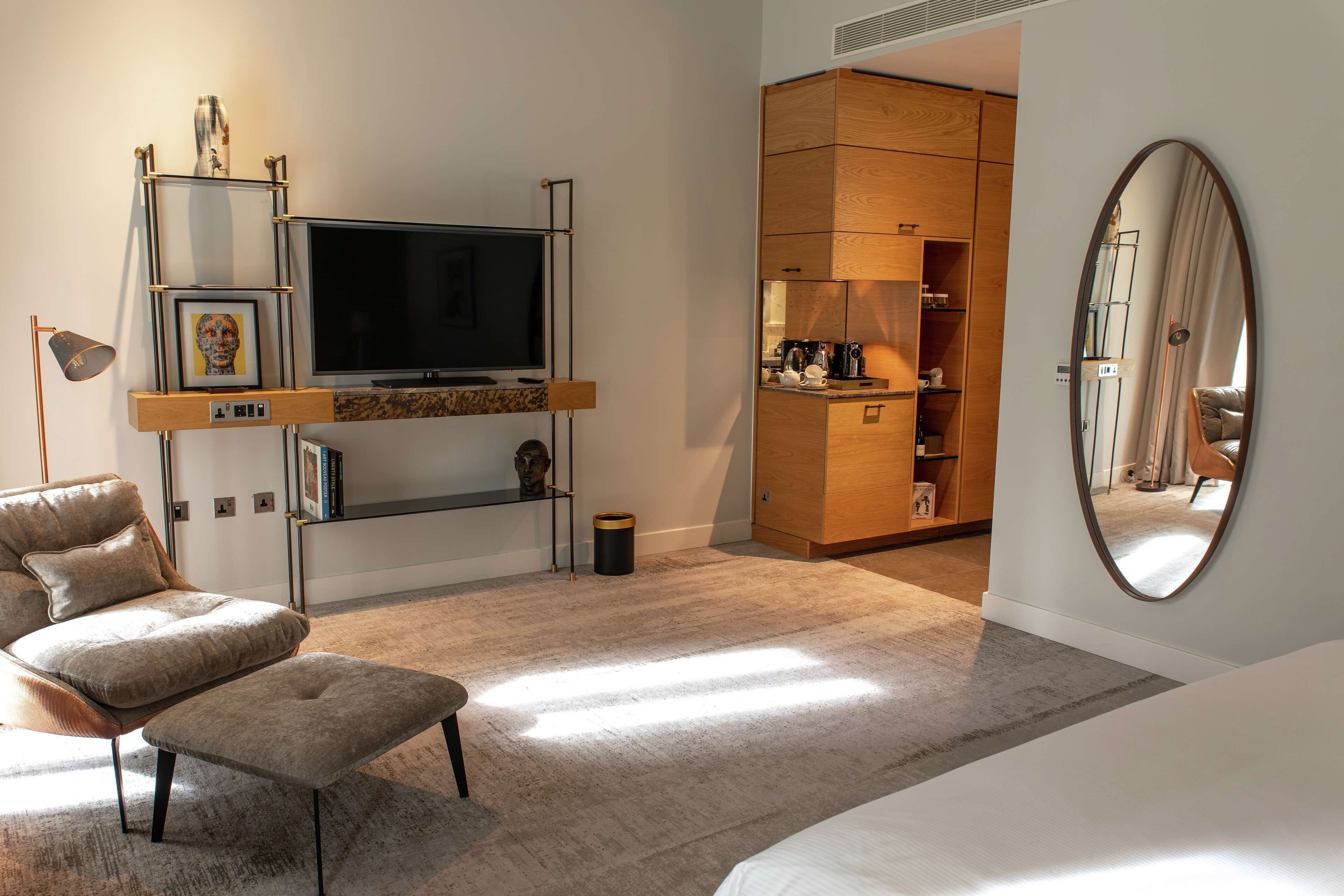 A modern living room with a flat-screen TV, a sofa, an ottoman, a wooden cabinet, and a large mirror.