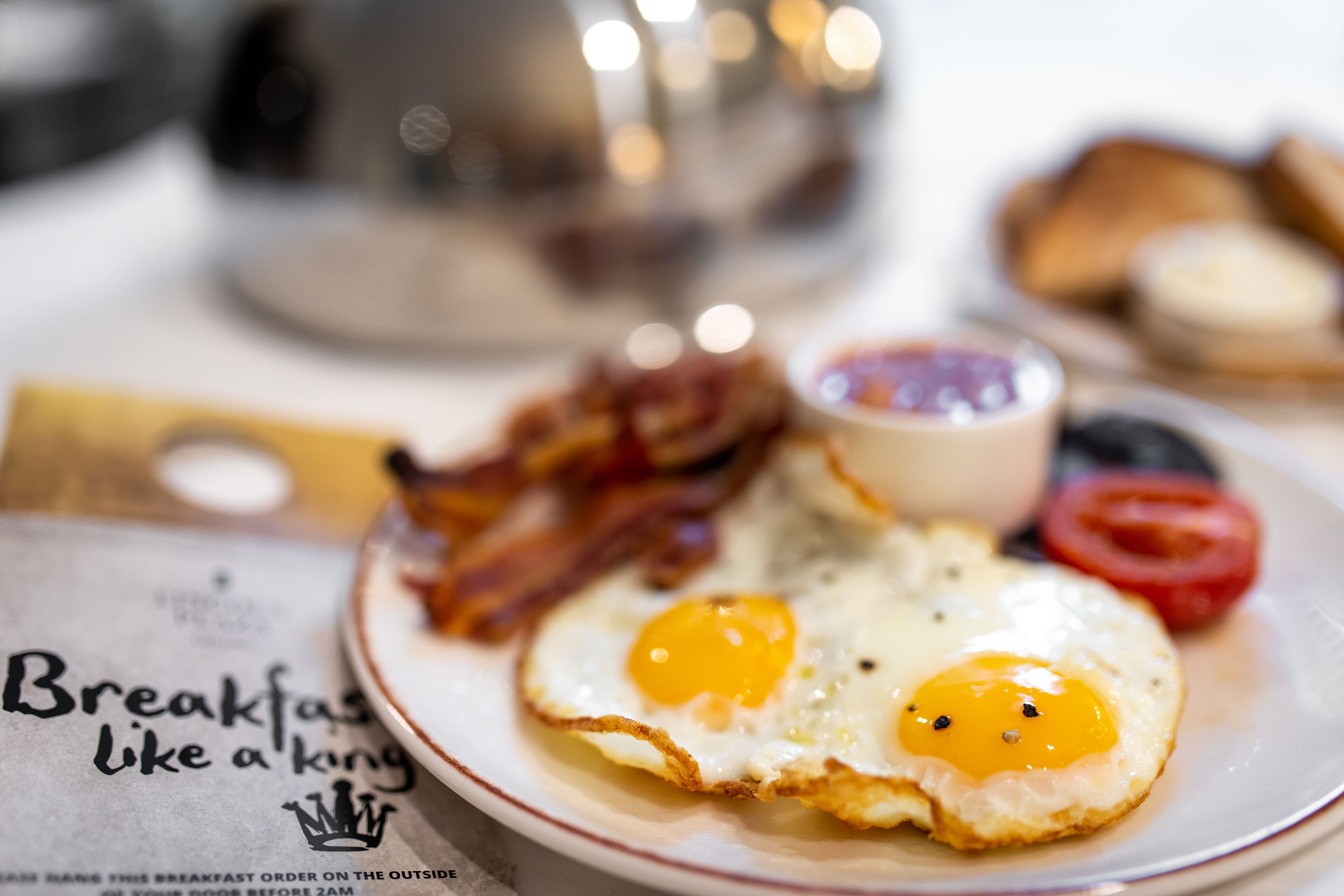 Une assiette de petit-déjeuner avec deux œufs au plat, du bacon et une tranche de tomate.