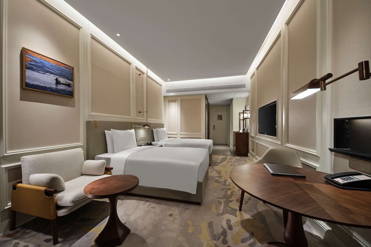 Ein Hotelzimmer mit einem Bett, einem Sofa, einem kleinen Tisch, einem Fernseher und einem Schreibtisch mit Stuhl.