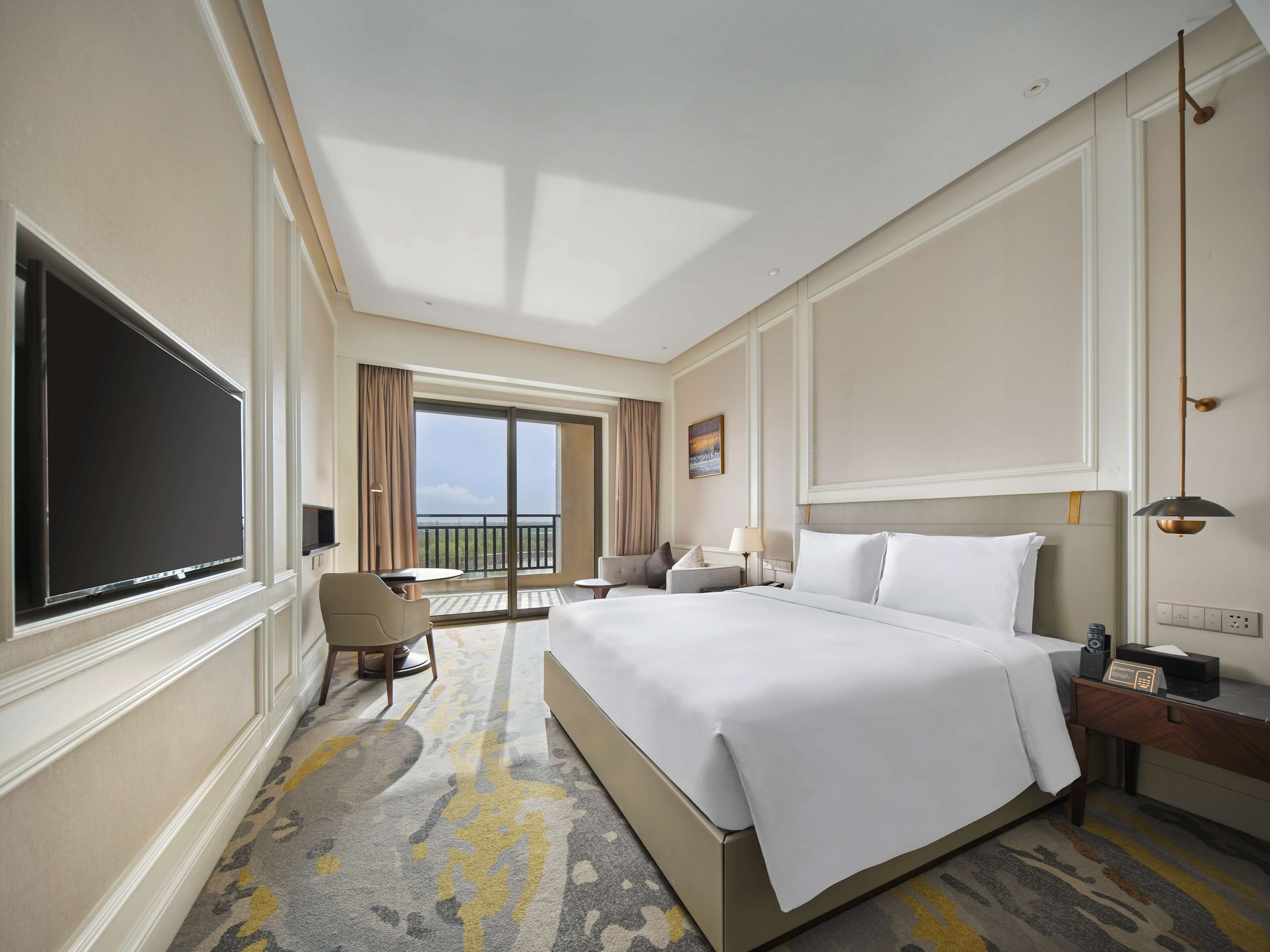 Habitación de hotel con una cama grande, un televisor de pantalla plana, un escritorio con lámpara y vistas al exterior.