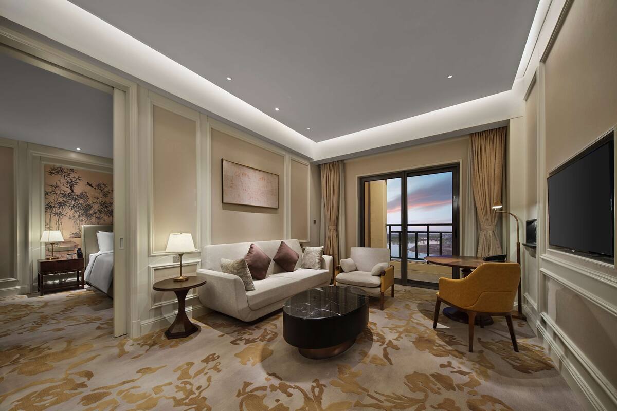 Ein geräumiges Hotelzimmer mit einer großen Couch, einem runden Couchtisch, einem Fernseher und einem Balkon mit Blick.