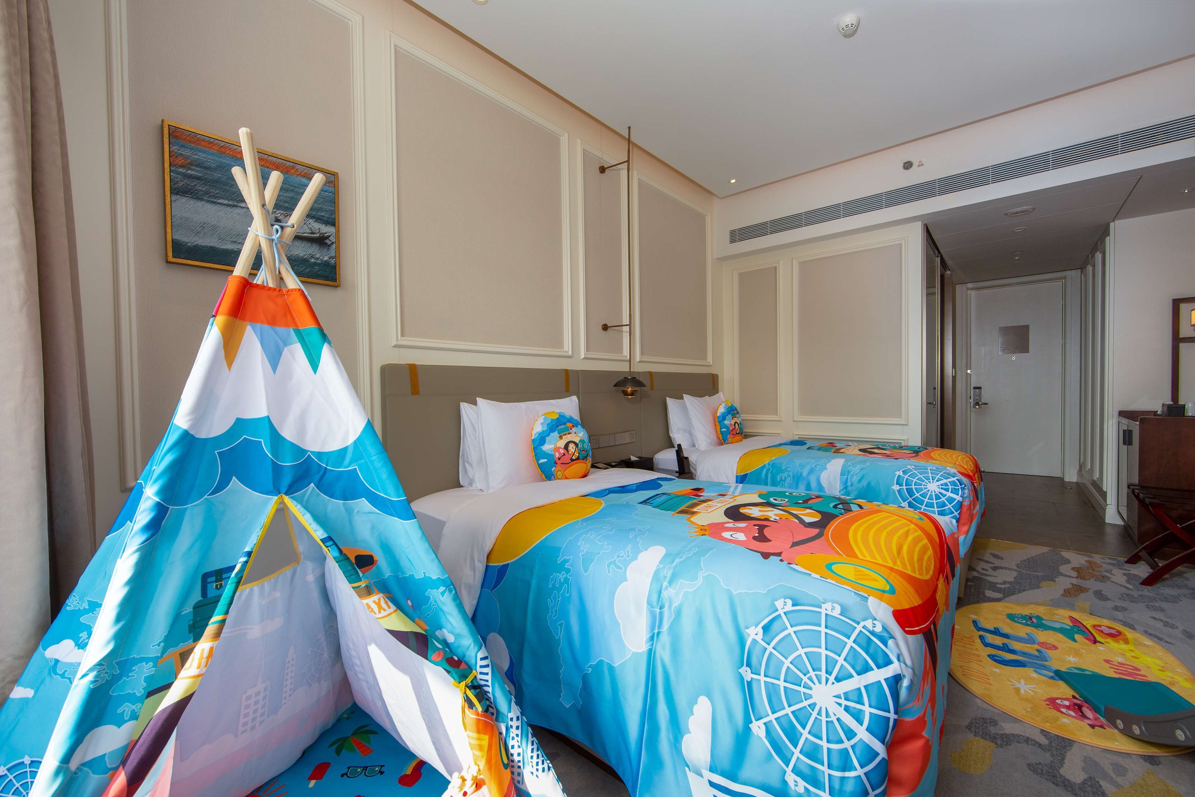 Habitació d'hotel amb dos llits, un llençol de llit colorit, un xalet petit i un quadre a la paret.