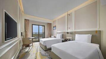 A hotel room with two beds, a TV, a desk, and a balcony with a view.