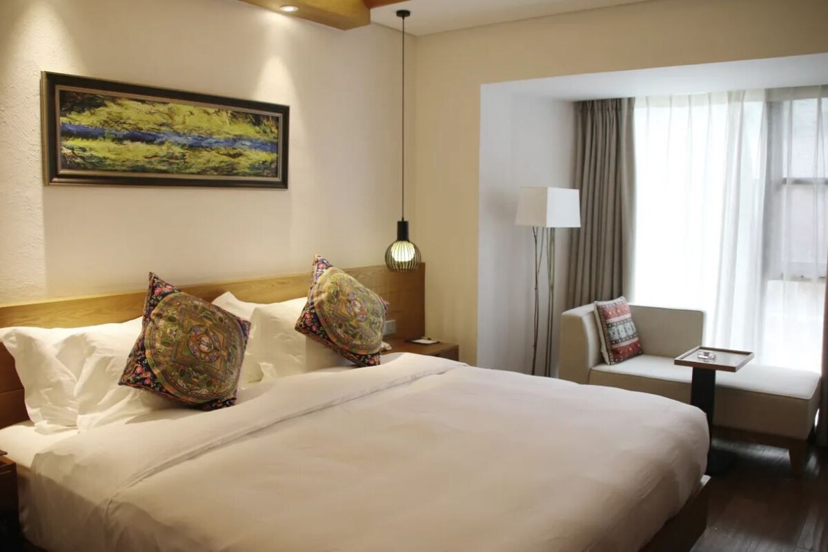 A hotel room with a large bed, a sofa, a desk, and a window with curtains.