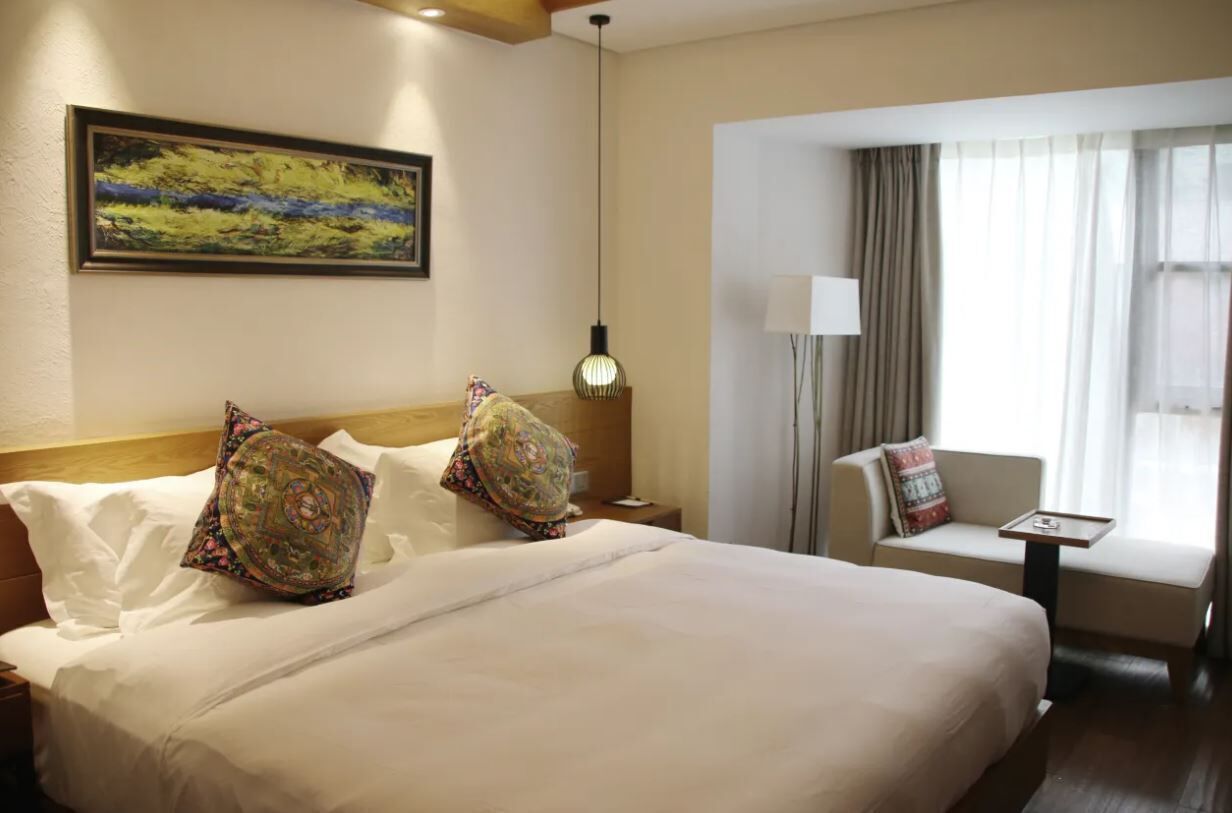 A hotel room with a large bed, a sofa, a desk, and a window with curtains.