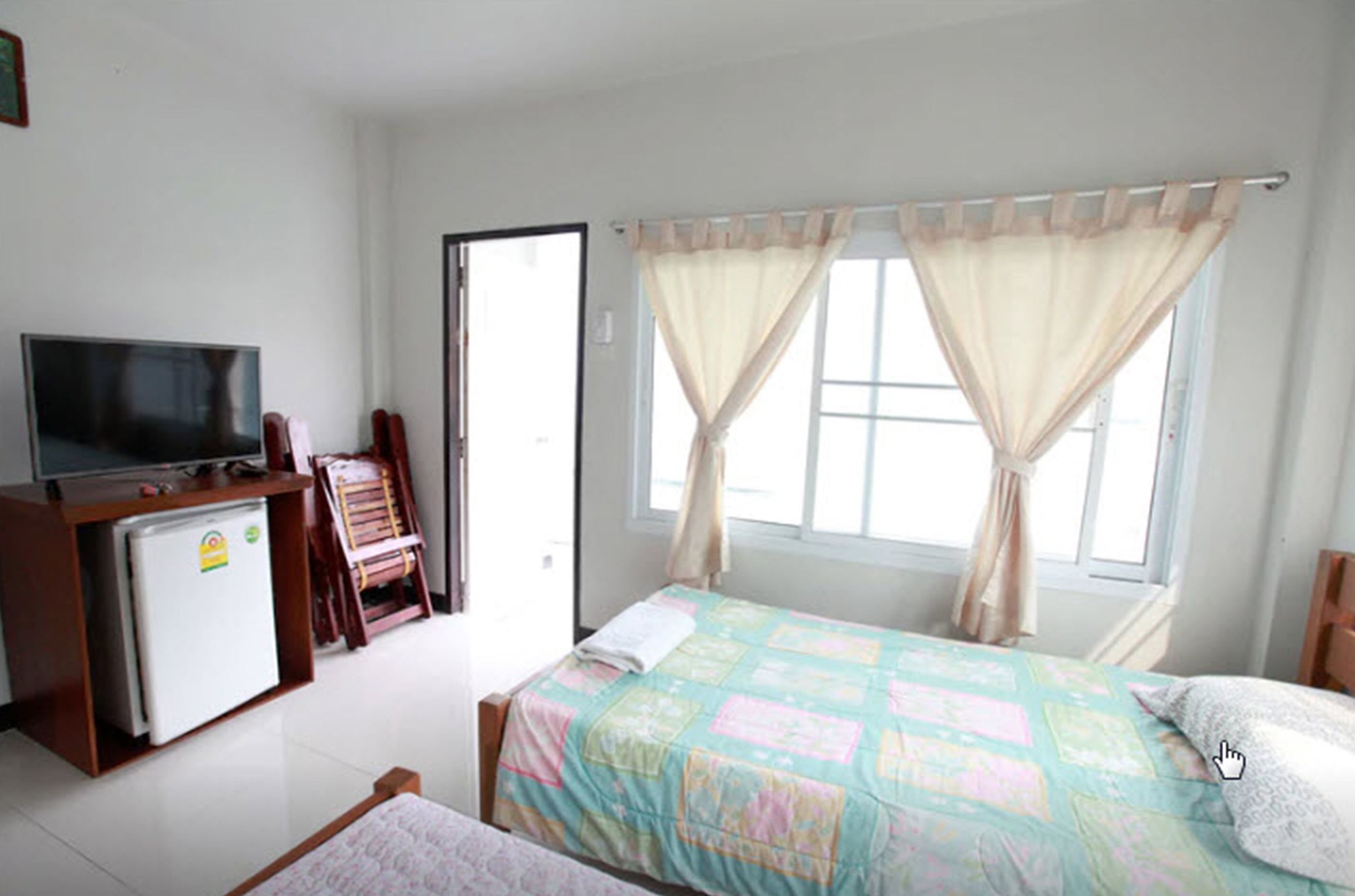 A bedroom with a bed, a television, a small refrigerator, and a window with curtains.
