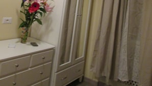 A room with a white wardrobe, a dresser with drawers, a vase with flowers, and a curtain. - Trevi Elegance Suite (Rome)