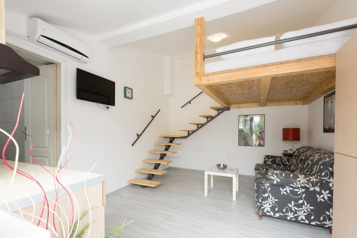A modern living room with a wooden staircase, a flat-screen TV, and a sofa.