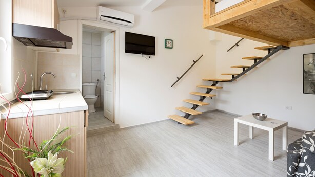 A modern kitchen with a built-in stove, a white countertop, and a wooden staircase leading to a loft area.