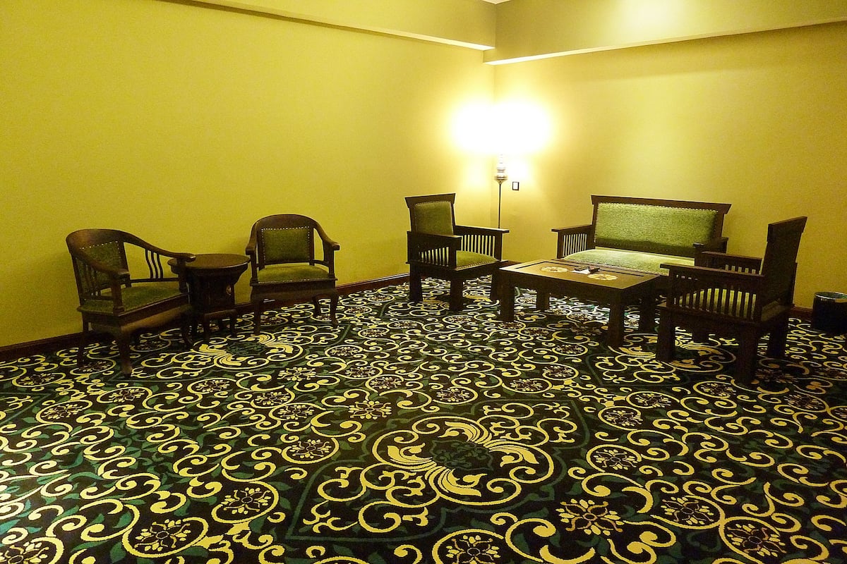Una habitación con alfombra estampada, muebles de madera y una lámpara fijada a la pared.