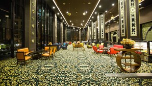 Un vestíbulo de hotel con alfombra estampada, zonas de estar y un mostrador de recepción.