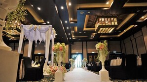Montaje formal para un evento con un pasillo blanco, sillas negras y centros de mesa florales.