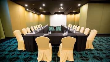 Un salón de conferencias con una larga mesa, sillas y una pantalla para proyector.