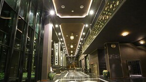 Un pasillo de hotel moderno con suelo de baldosas blancas y negras reflectantes, iluminación empotrada y paneles decorativos en la pared.