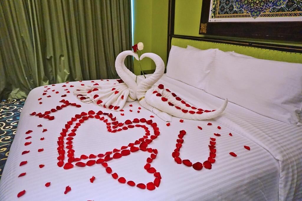 Een bed met een hartvormige bloemstuk van rozenblaadjes en een zwaan-vormige handdoek.