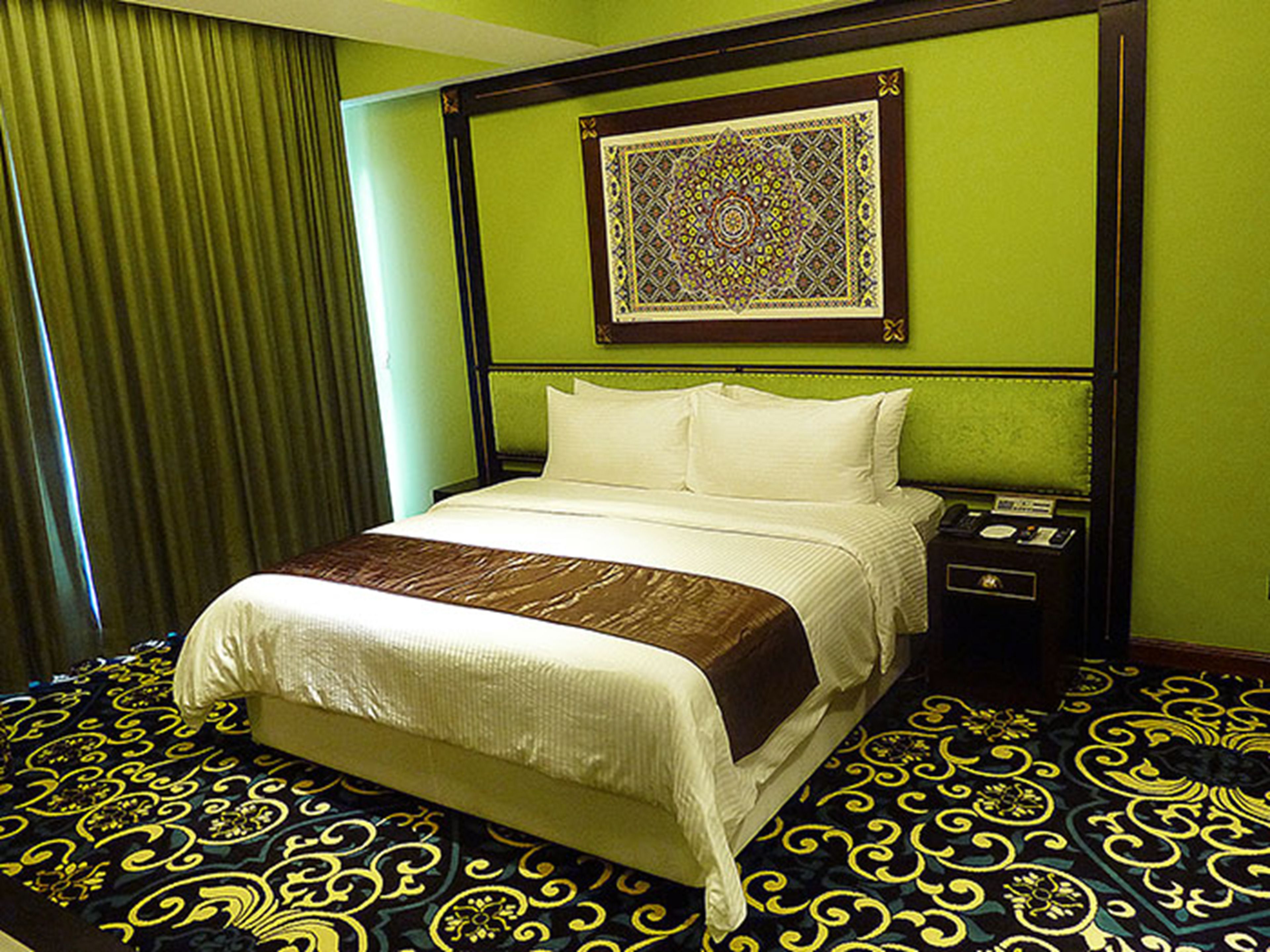 A hotel room with a bed, a nightstand, a telephone, and a decorative wall hanging.