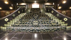 Una imponente escalera con barandillas ornamentadas y peldaños estampados que llevan a un balcón.