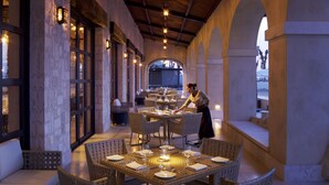 Un restaurante con mesas dispuestas para comer, un camarero atendiendo una mesa y vistas al exterior a través de ventanales arqueados.