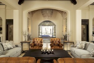 Un salón espacioso con sillones de cuero, una mesa de centro y un amplio arco que da a un espacio exterior luminoso.