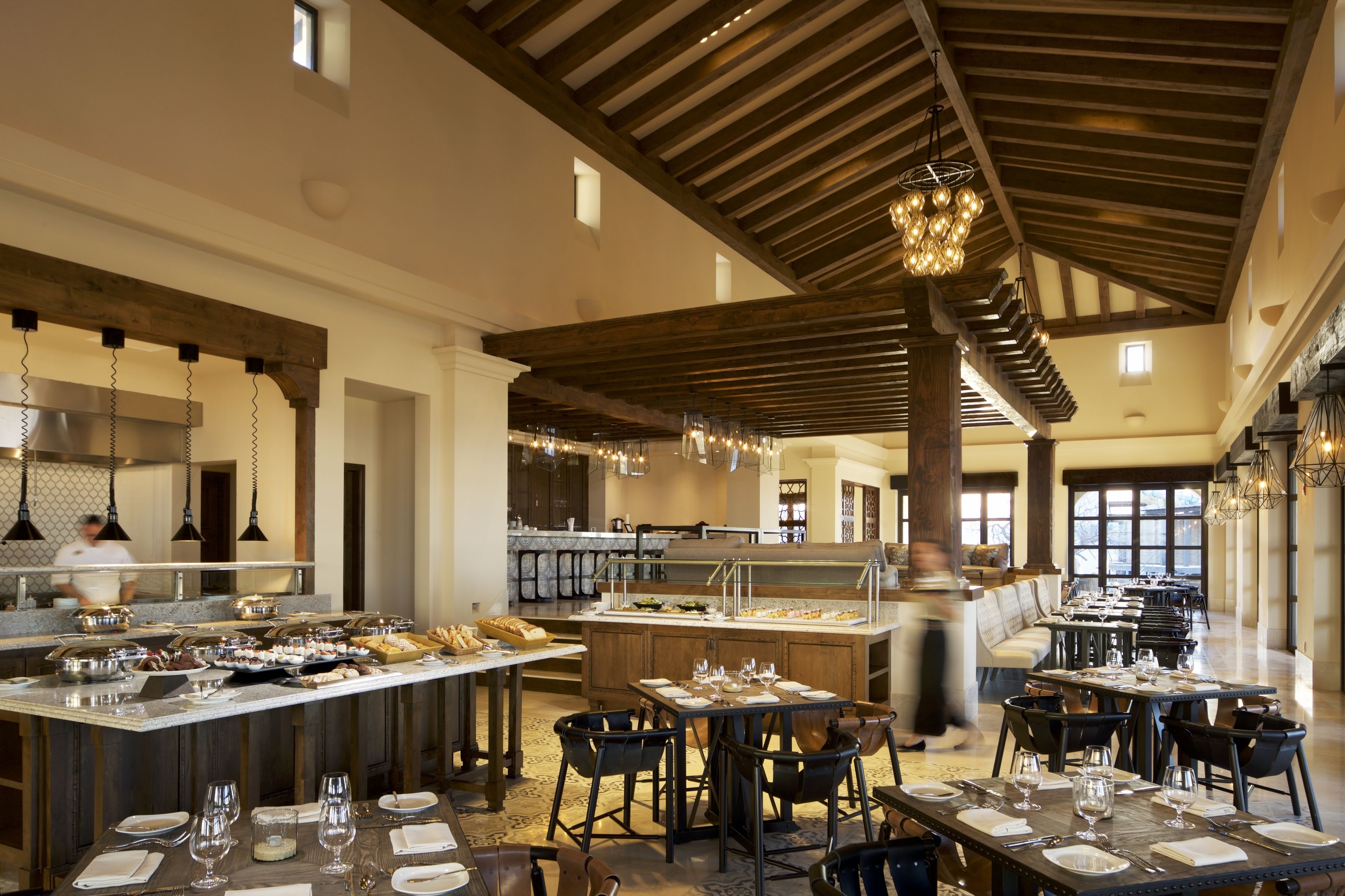 Ein großzügiges Restaurant mit hohen Decken, freiliegenden Balken und einer zentralen Insel mit Speisen und Getränken.