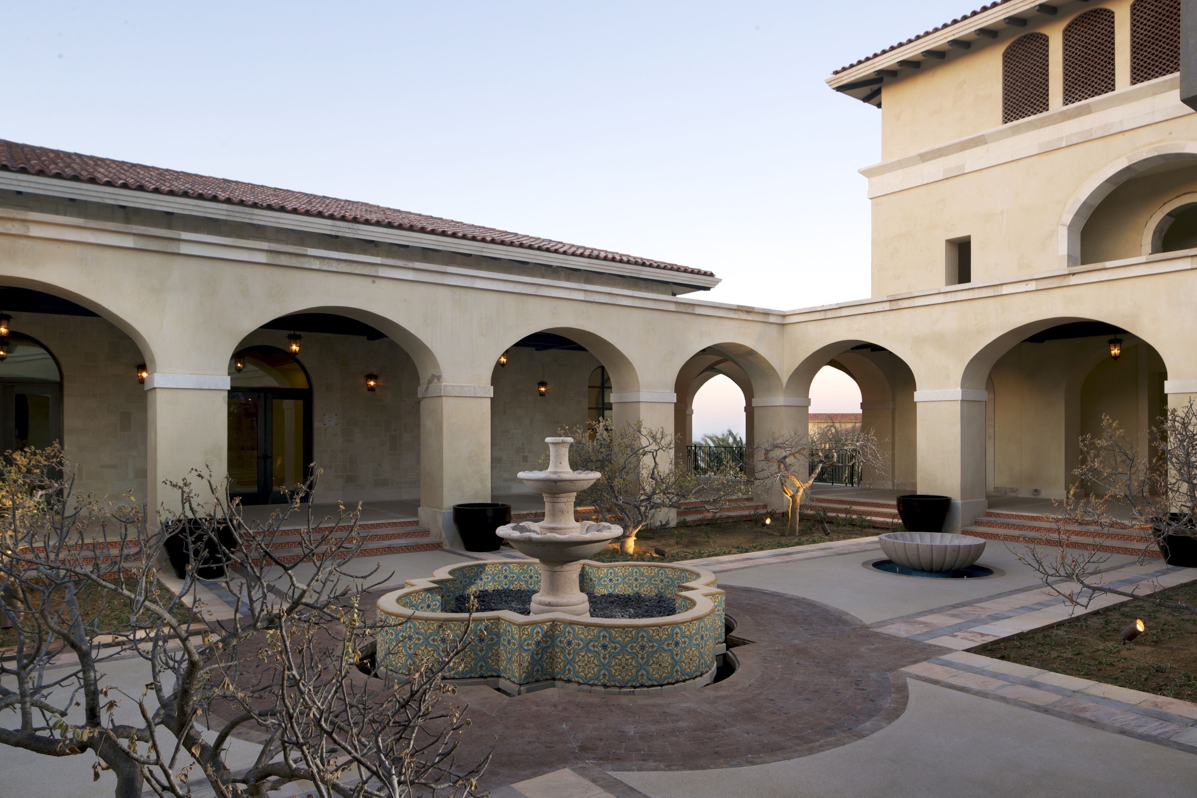 A courtyard with a central fountain, surrounded by arches and a building with a tiled roof.