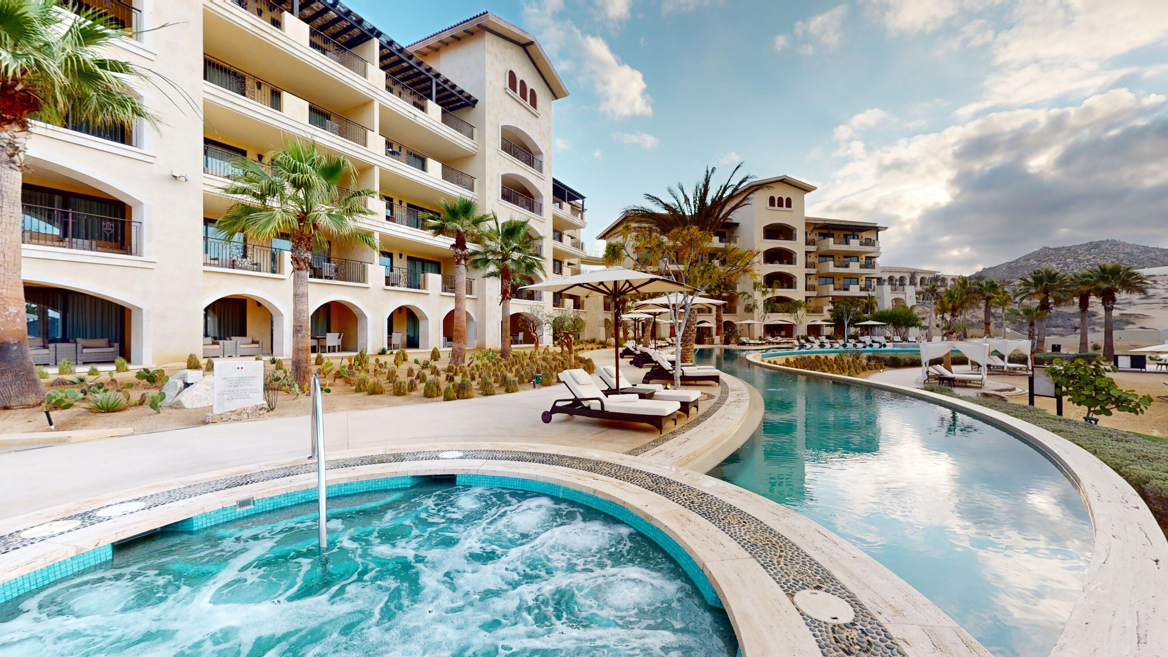 A resort with a large pool, multiple balconies, and palm trees.
