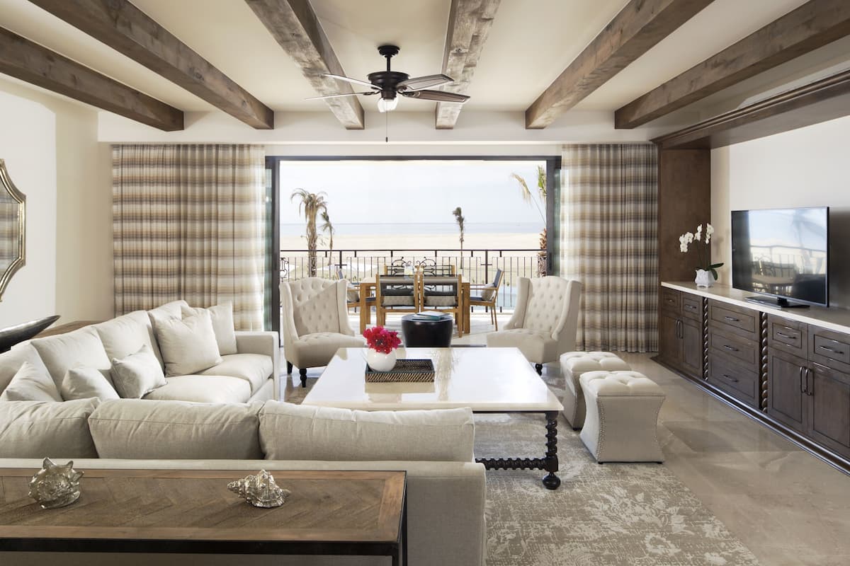 Een ruime woonkamer met een grote bank, een salontafel en een televisie. Er is een balkon met uitzicht op het strand.