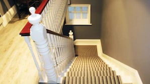 Een trap met een witte balustrade en een rode leuning, die uitkomt op een plateau met een klein raam.