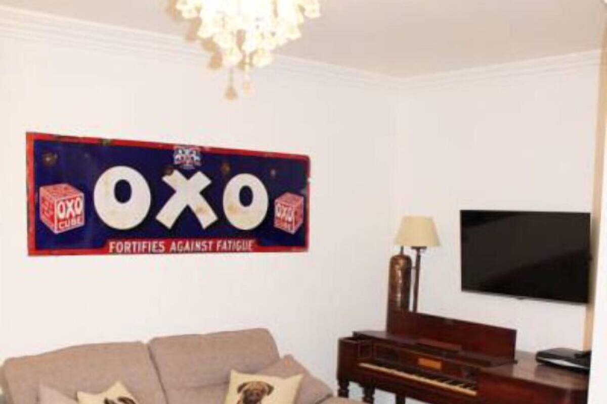 Een woonkamer met een beige bank, een houten piano, een televisie en een kroonluchter.